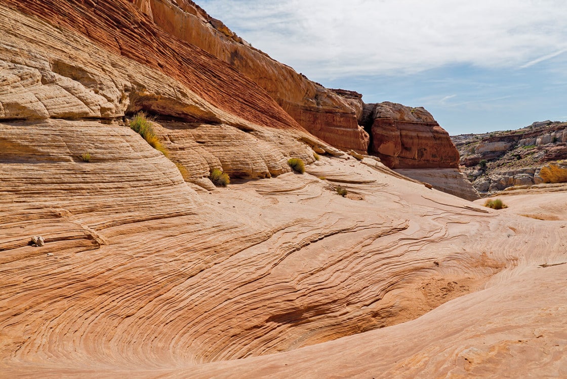 Unique sandstone formations layer intricately with sparse vegetation at Under Canvas Lake Powell - Grand Staircase.