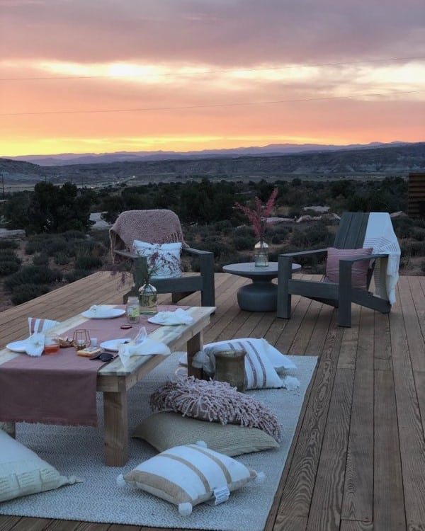 An outdoor wooden deck features cozy seating and a table set for an Under Canvas event, overlooking a vast landscape.