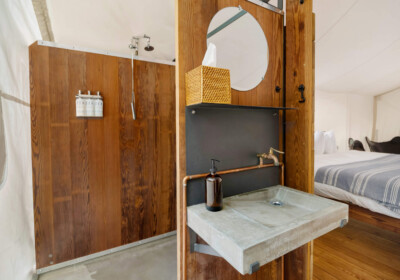 A private bathroom with a sink, shower, and flushing toilet inside an Under Canvas tent suite.