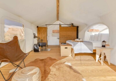 The Stargazer Tent interior with a king-size bed and a wood-burning stove at an Under Canvas glamping resort.