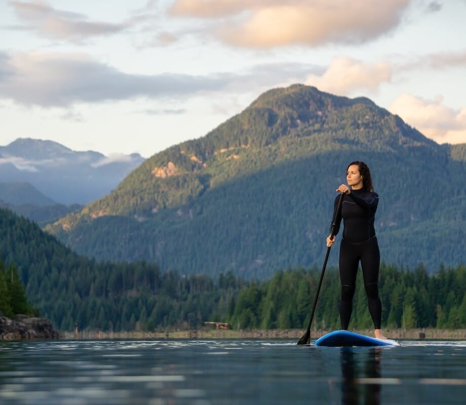 Adventurous Girl on a Paddle Board is paddling in a calm lake with mountains in the background during a colorful summer sunset. Taken in Stave Lake near Vancouver, BC, Canada.