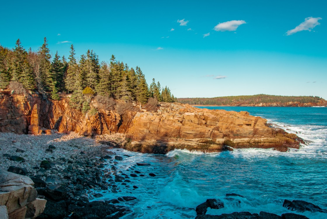 A rocky formation with pine trees and blue waters at Acadia National Park.