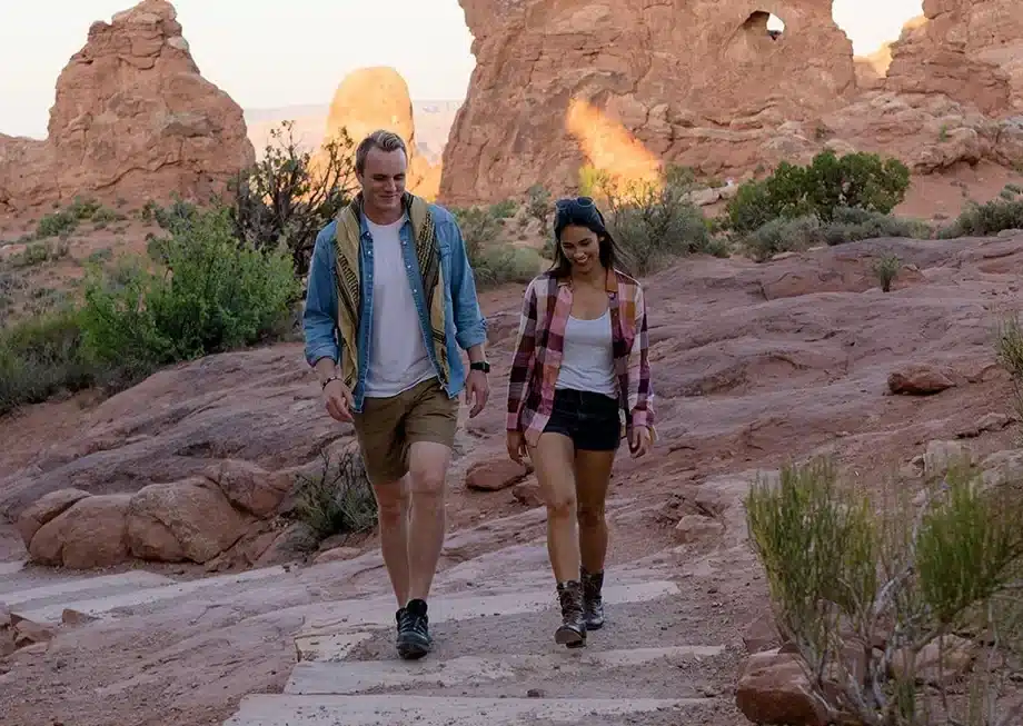 Two people walk in red rock landscapes within one of Utah's national parks.