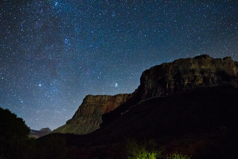 A red rock formation stands silhouetted against a vast, starry night sky, showcasing stargazing in the Southwest U.S.