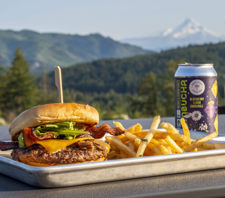 Cheeseburge with toppings, fries and a beverage sitting on a table with views of Mount Hood at Under Canvas Columbia River Gorge