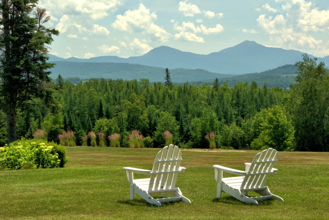 Inviting and restful scenic vista, Whitefield, New Hampshire. White lawn chairs overlooking hillside of lush evergreen trees framed by distant mountains in the Presidential Range.