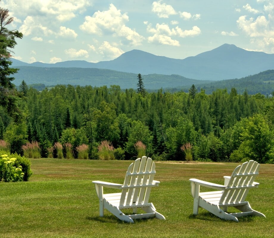 Inviting and restful scenic vista, Whitefield, New Hampshire. White lawn chairs overlooking hillside of lush evergreen trees framed by distant mountains in the Presidential Range.