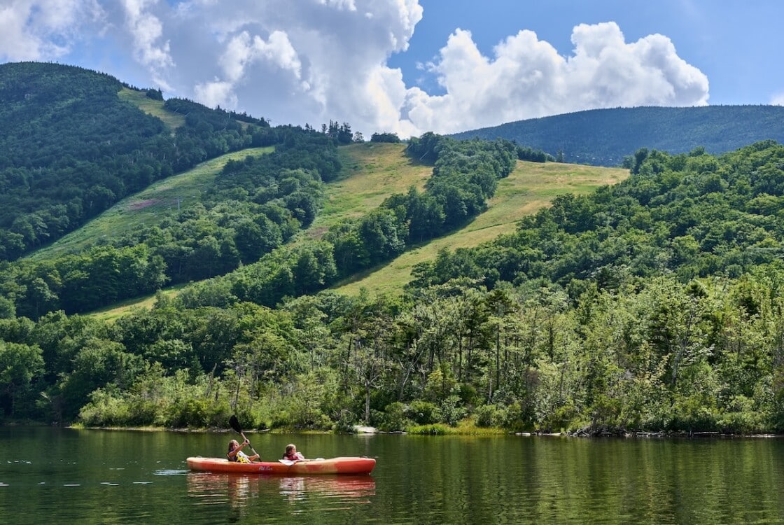 Franconia, NH USA - August 5, 2022: Kayakers on Echo Lake. Behind are ski trails of Cannon Mountain Ski resort in the summer time with a blue sky and dramatic clouds.