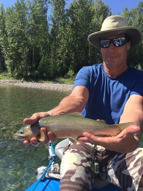 Man holding a trout he caught on a river.