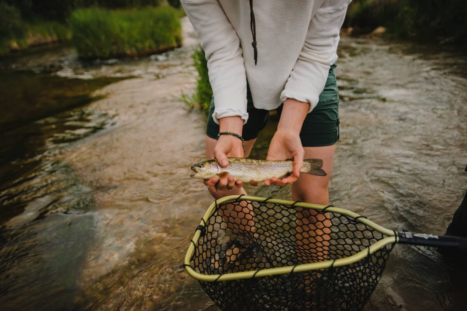 Man holding a trout he caught over a net.