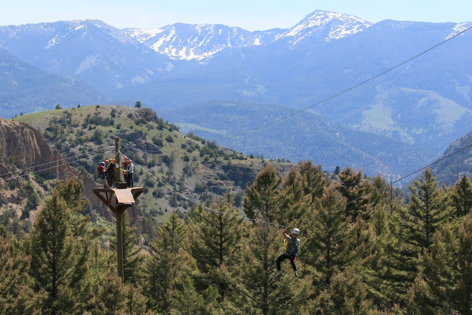 People riding a zipline in Paradise Valley, MT, with mountains in the background.