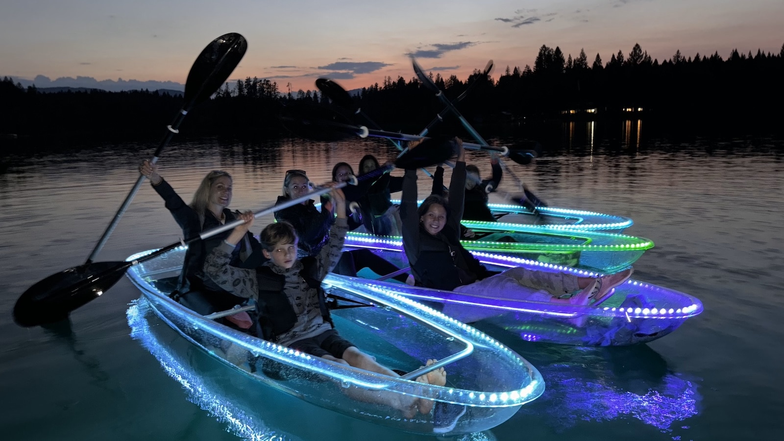 Group of friends in LED illuminated glass kayaks on Peterson lake in Glacier National Park.