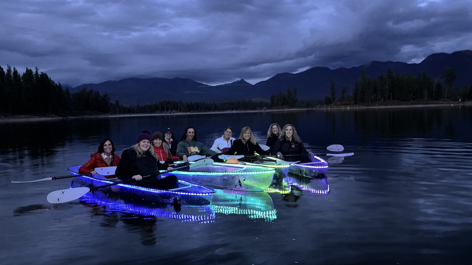 Group of friends in LED illuminated glass kayaks on Peterson lake in Glacier National Park.